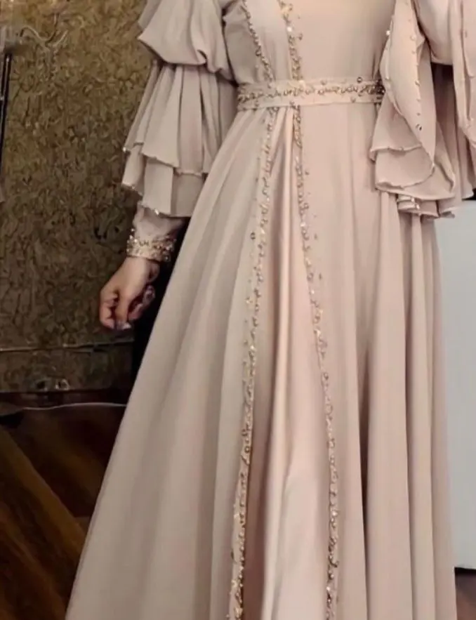 A woman wearing a beige layered sleeve abaya poses for a selfie with a cheerful expression