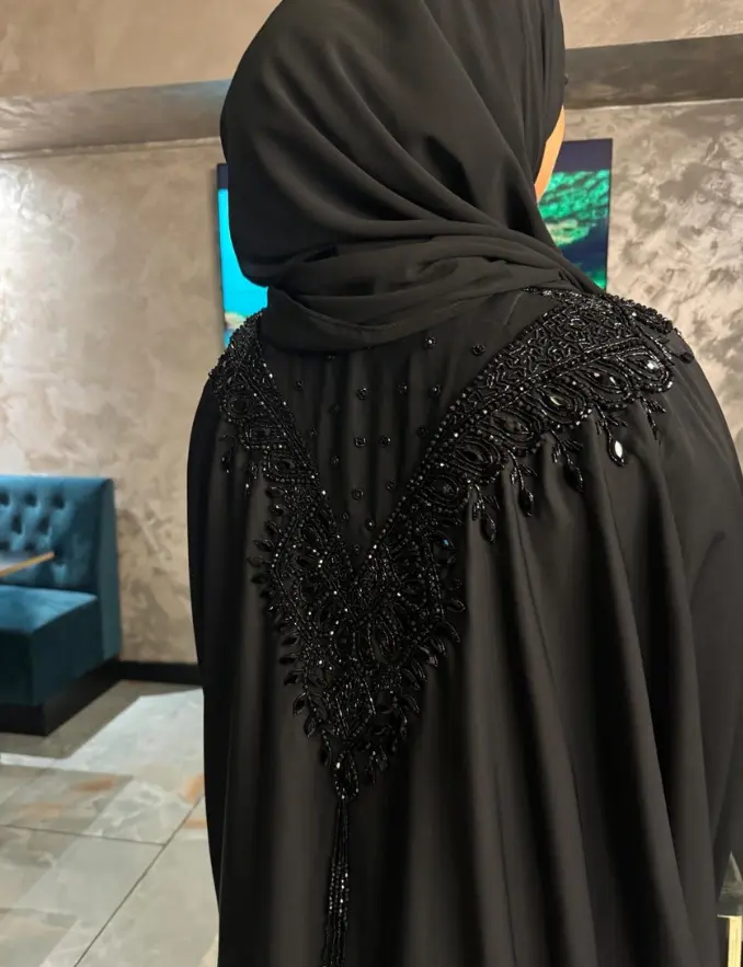  A woman wearing a black beaded shoulder abaya and a matching black veil, standing elegantly