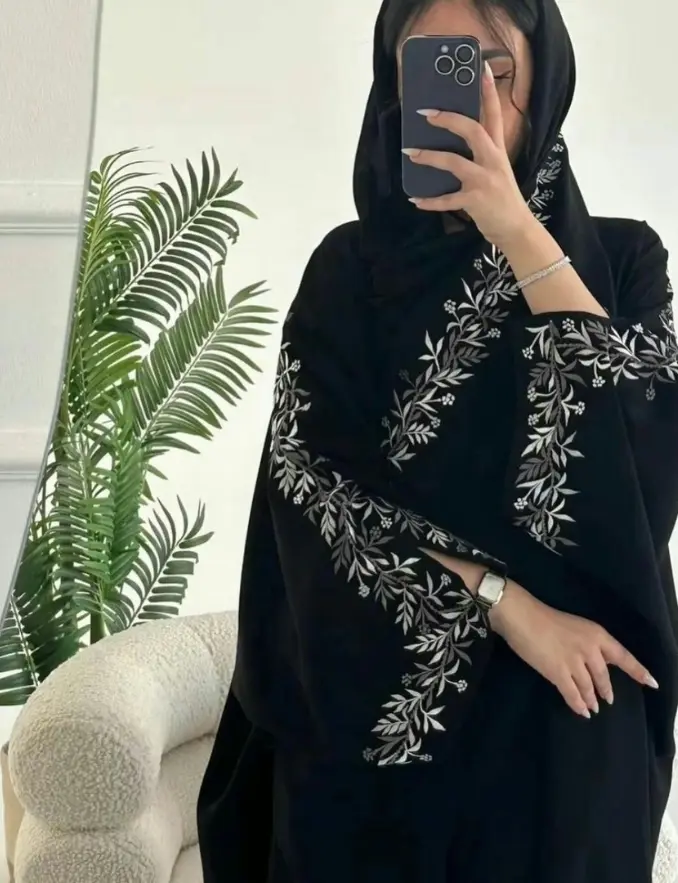 A woman in a black floral vine embroidered abaya, standing gracefully with a serene expression
