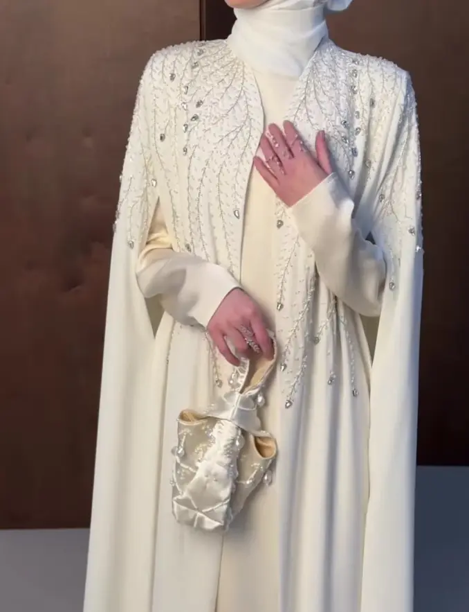  A woman in a white hijab and a matching white dress poses, showcasing a blend of modesty and style<br />

