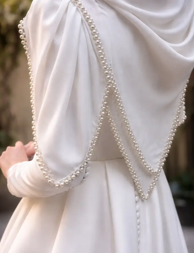 The back view of a woman in a white dress adorned with pearls, showcasing elegance and sophistication