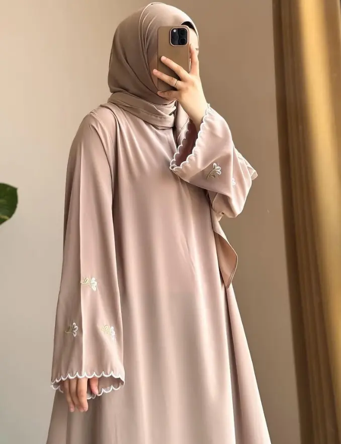 A woman in a beige Muslim dress takes a selfie, smiling and showcasing her stylish nude classic sleeve abaya