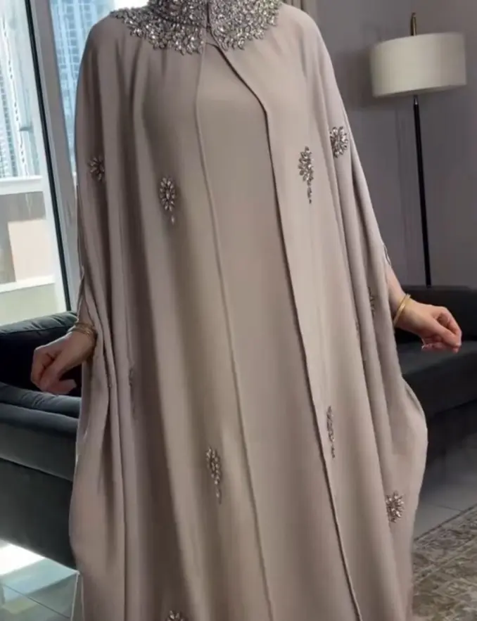 A woman wearing a taupe embellished batwing sleeve abaya, showcasing elegant design and modest fashion